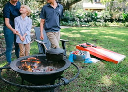 Kids roasting hot dogs around the fire kettle